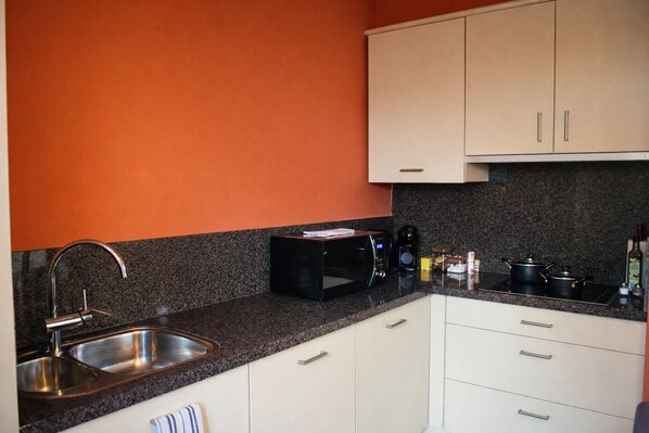 A kitchen with a granite countertop, stainless steel sink, white cabinets, and a microwave.