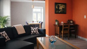 Un salon avec un canapé noir, une table basse en verre et un coin repas comprenant une table et des chaises.