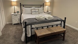 Une chambre à coucher bien rangée, avec un lit, des lampes de chevet, une table de chevet, un banc et une fenêtre.