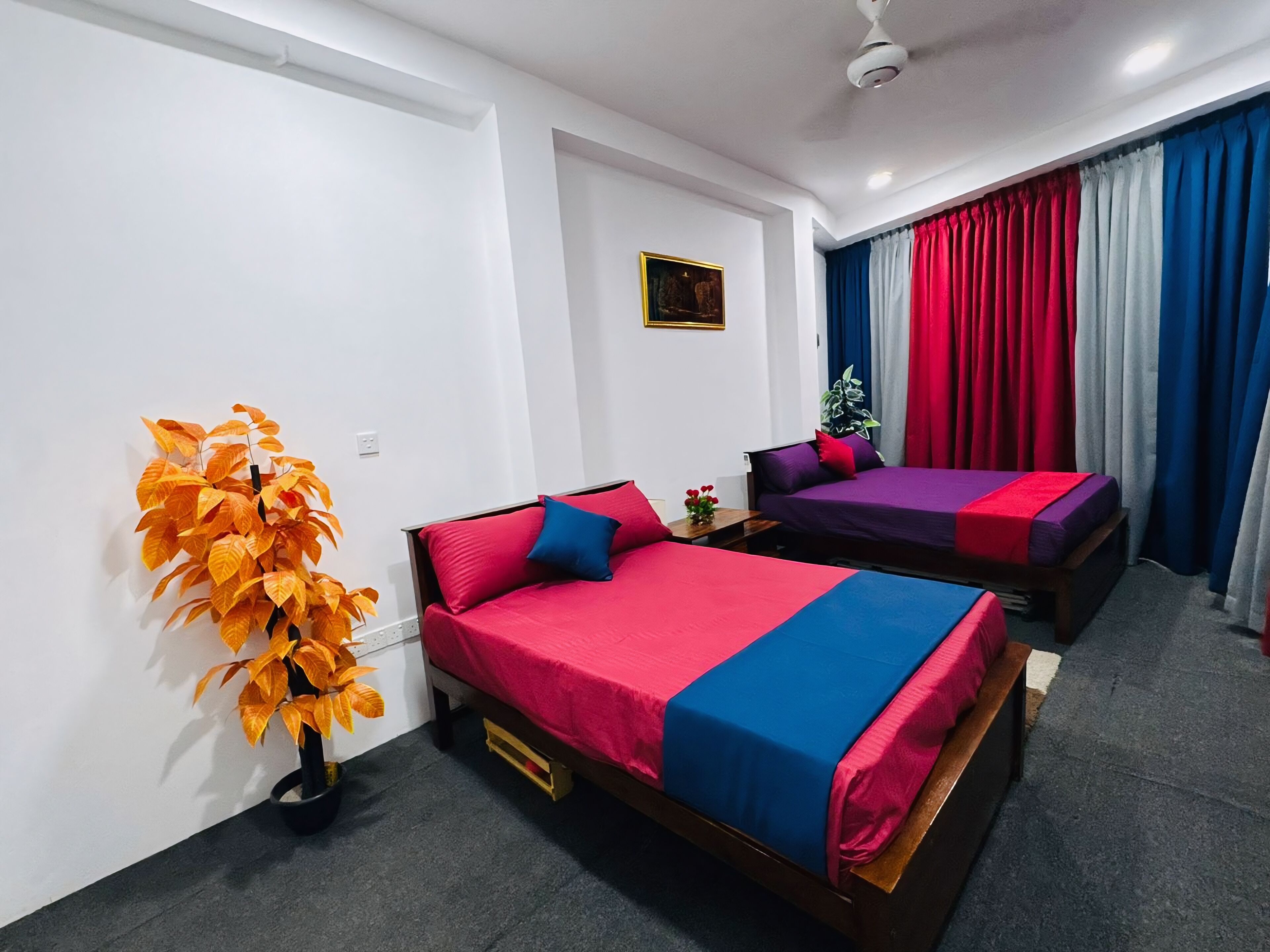 A hotel room with two beds, a ceiling fan, a wall-mounted painting, and a window with curtains.