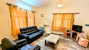 A living room with a black sofa, a wooden coffee table, and a television. - A 2 bedroom villa, with full self catering kitchen set in a quaint Goan village. (Navelim)
