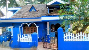 A blue house with a tiled roof, white fence, and a bicycle parked outside. - A 2 bedroom villa, with full self catering kitchen set in a quaint Goan village. (Navelim)