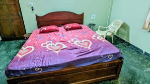 A bed with a wooden headboard, a purple and pink bedspread with heart patterns, a white plastic chair, and a green marble floor. - A 2 bedroom villa, with full self catering kitchen set in a quaint Goan village. (Navelim)