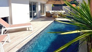 Una casa moderna con piscina, mobiliario exterior y un gran paraguas.