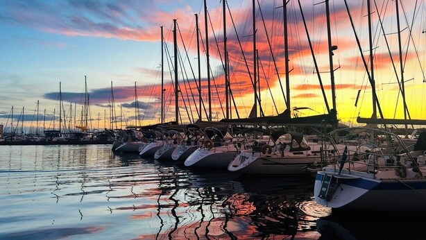 Marina con varios veleros amarrados, reflejando el cielo al atardecer.