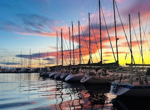Marina com vários veleiros atracados, refletindo o céu do pôr do sol.