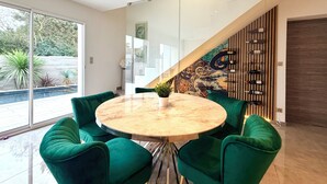 Un comedor moderno con una mesa redonda y sillas tapizadas de verde, una partición de vidrio y una escalera con un mural decorativo.