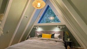 A bedroom with a sloped ceiling, a bed with striped bedding, a small bedside table, and a hanging light fixture. - Das-Bergheim.de A stylish vacation home in Chiemgau! (Siegsdorf)
