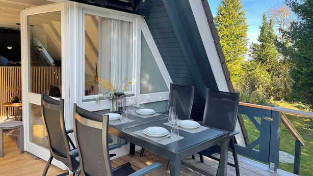 An outdoor dining area with a table set for two, chairs, and a view of the garden. - Das-Bergheim.de A stylish vacation home in Chiemgau! (Siegsdorf)