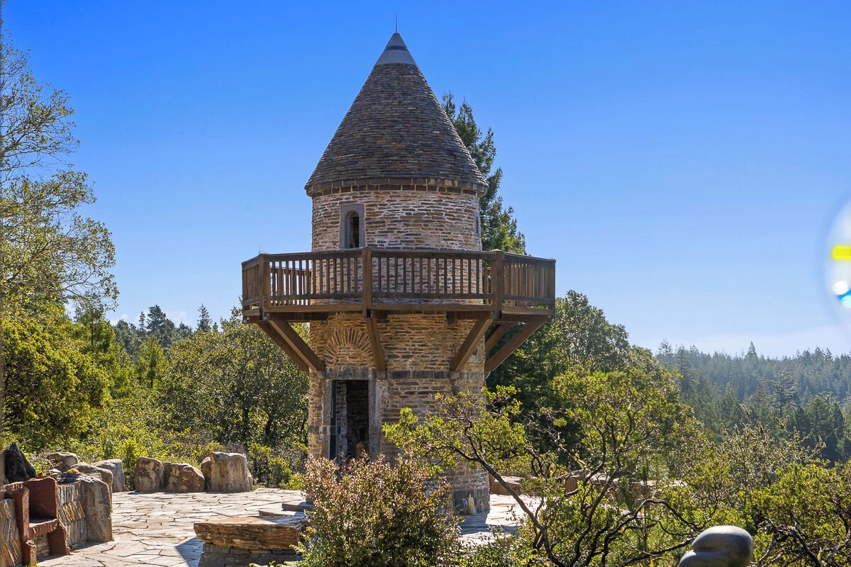 A stone tower with a wooden balcony, surrounded by trees and rocks.