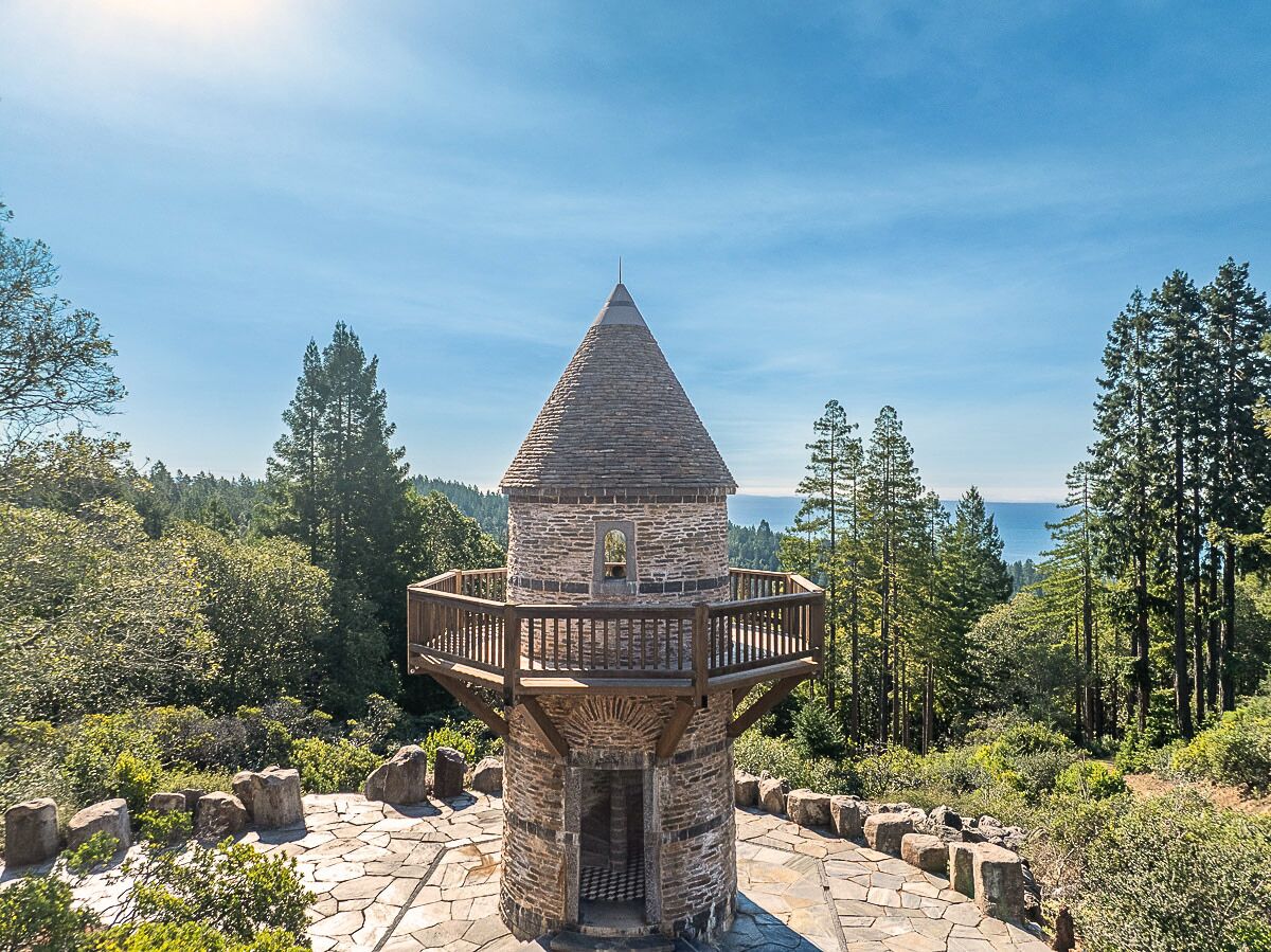 A stone observation tower with a wooden balcony, surrounded by trees and a clear sky.