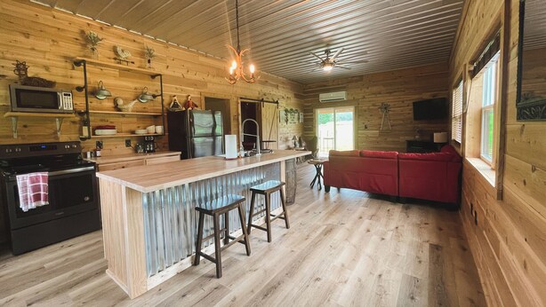 Amplio interior de cabaña con detalles de madera, cocina con electrodomésticos modernos, sofá rojo y zona de bar.