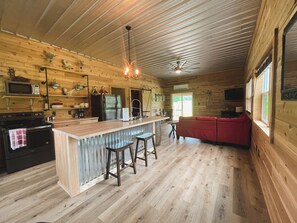 A spacious cabin interior with a wooden interior, a kitchen with modern appliances, a red sofa, and a bar area. - The Shawnee Farmhouse - 3-bedroom, 2 bathroom, cabin the heart of Southern IL (Golconda)