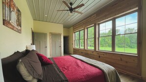 Un dormitorio con cama, ventilador de techo y amplias ventanas.