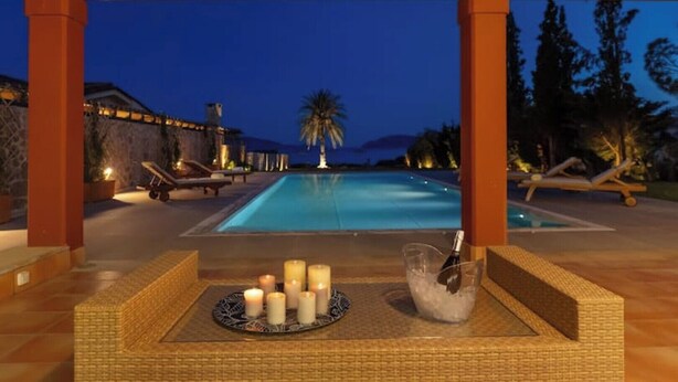 A poolside area with lounge chairs, a table with candles, and a view of the pool at dusk. - Private Beachfront Villa, Experience beauty, luxury and serenity, all in one. (Θερμησία)