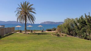 A backyard with a palm tree, two umbrellas, and a view of the sea. - Private Beachfront Villa, Experience beauty, luxury and serenity, all in one. (Θερμησία)