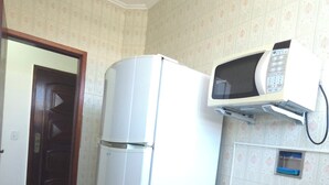 A compact kitchen with a refrigerator, microwave, coffee maker, and a cabinet with a screen door.