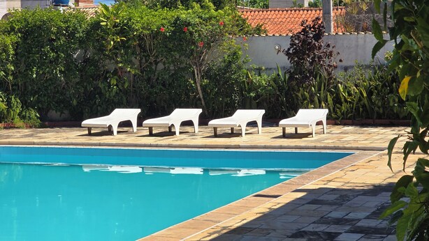 A swimming pool with four white lounge chairs aligned along the edge.
