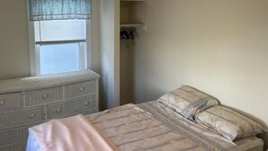 A bedroom with a bed, a dresser, a window with a curtain, and a closet.