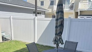 A patio with a round table and four chairs, an umbrella, and a white fence in the background.