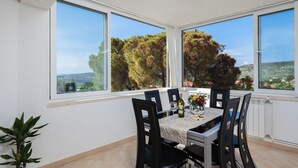 A dining area with a table set for four, large windows with a view of trees and hills, and a potted plant on the floor. - Villa with private pool, terrace and garden with fireplace (Nerezisca)