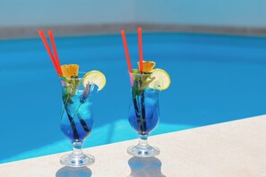 Zwei Cocktails mit Strohhalmen und Zitronenscheiben auf einem Tisch am Pool.