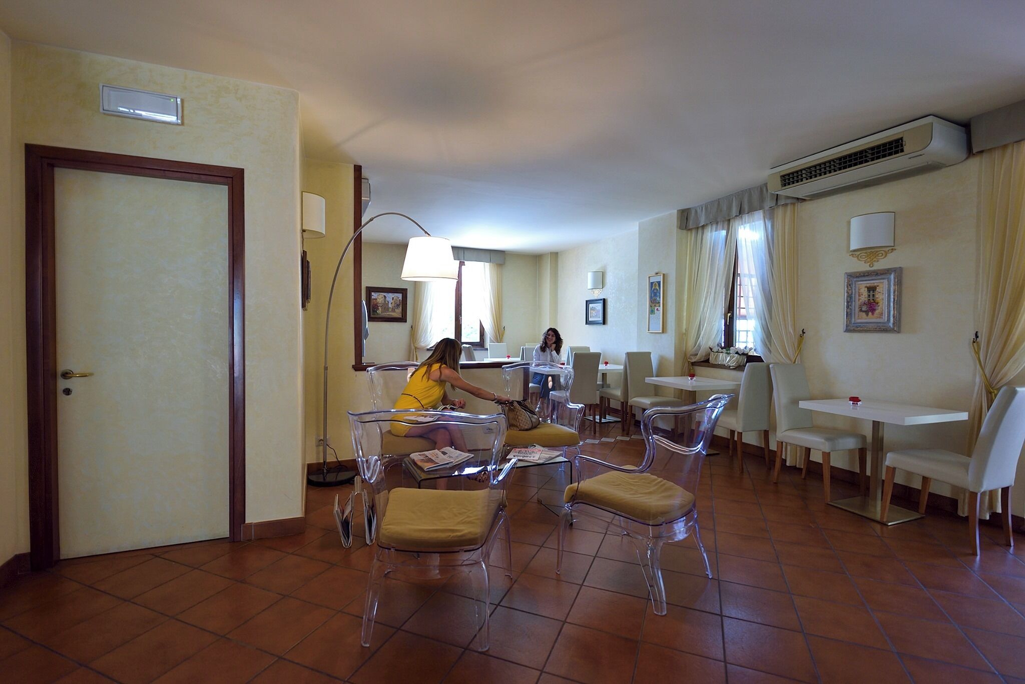 A dining area with clear chairs and a table, a door, and an air conditioning unit on the wall.