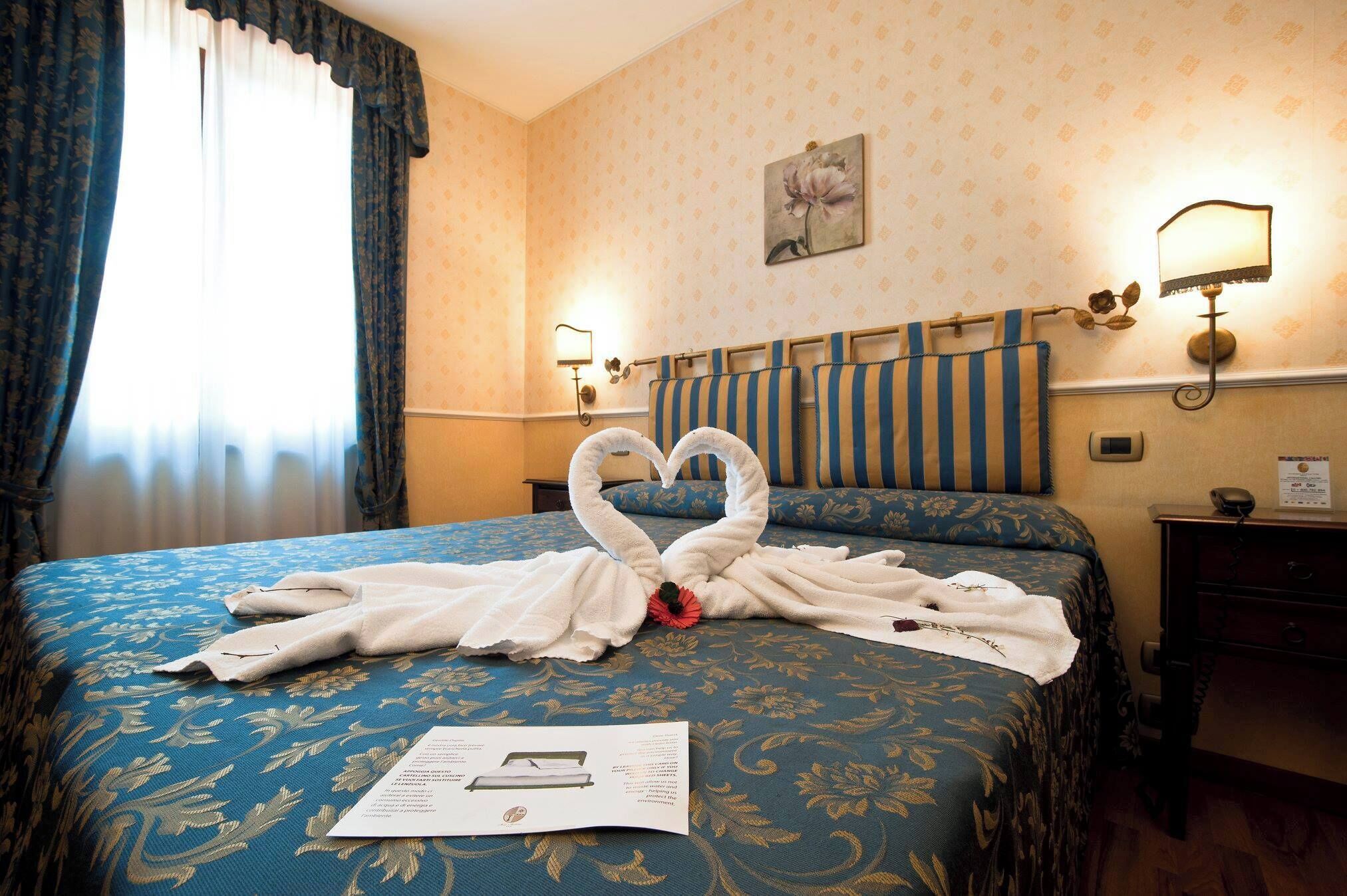 Een hotelkamer met een bed, een nachtkastje, een lamp en een raam met gordijnen.