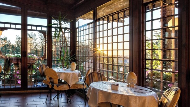 Un restaurante con mesas dispuestas para comer, ventanas amplias que dan a zonas verdes y un suelo de ladrillo.