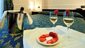 Una cama con una colcha azul estampada con flores, dos copas de vino blanco y un plato de fresas sobre una mesa.