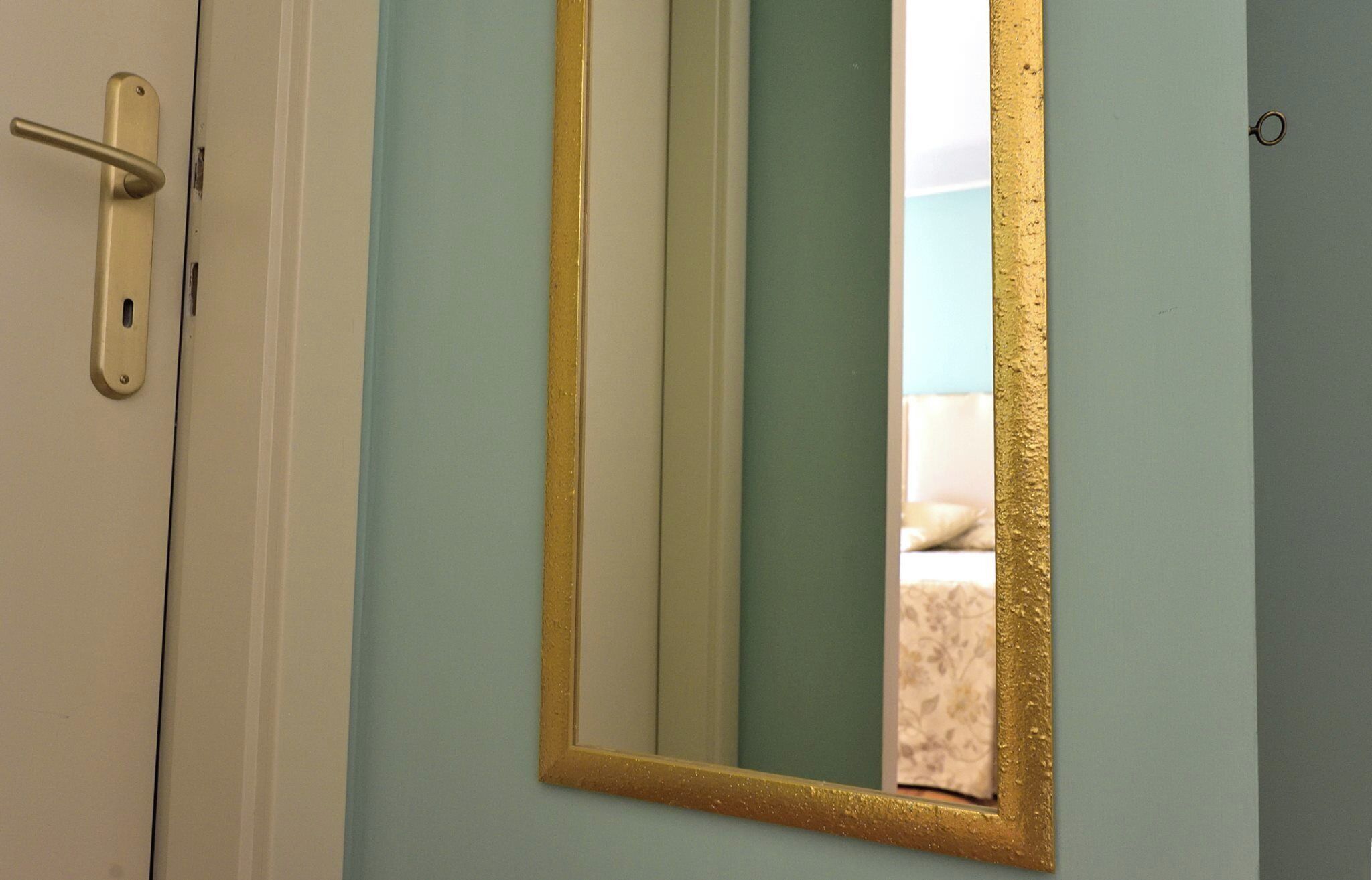 A door with a gold-framed mirror reflecting a room with a bed and a window.