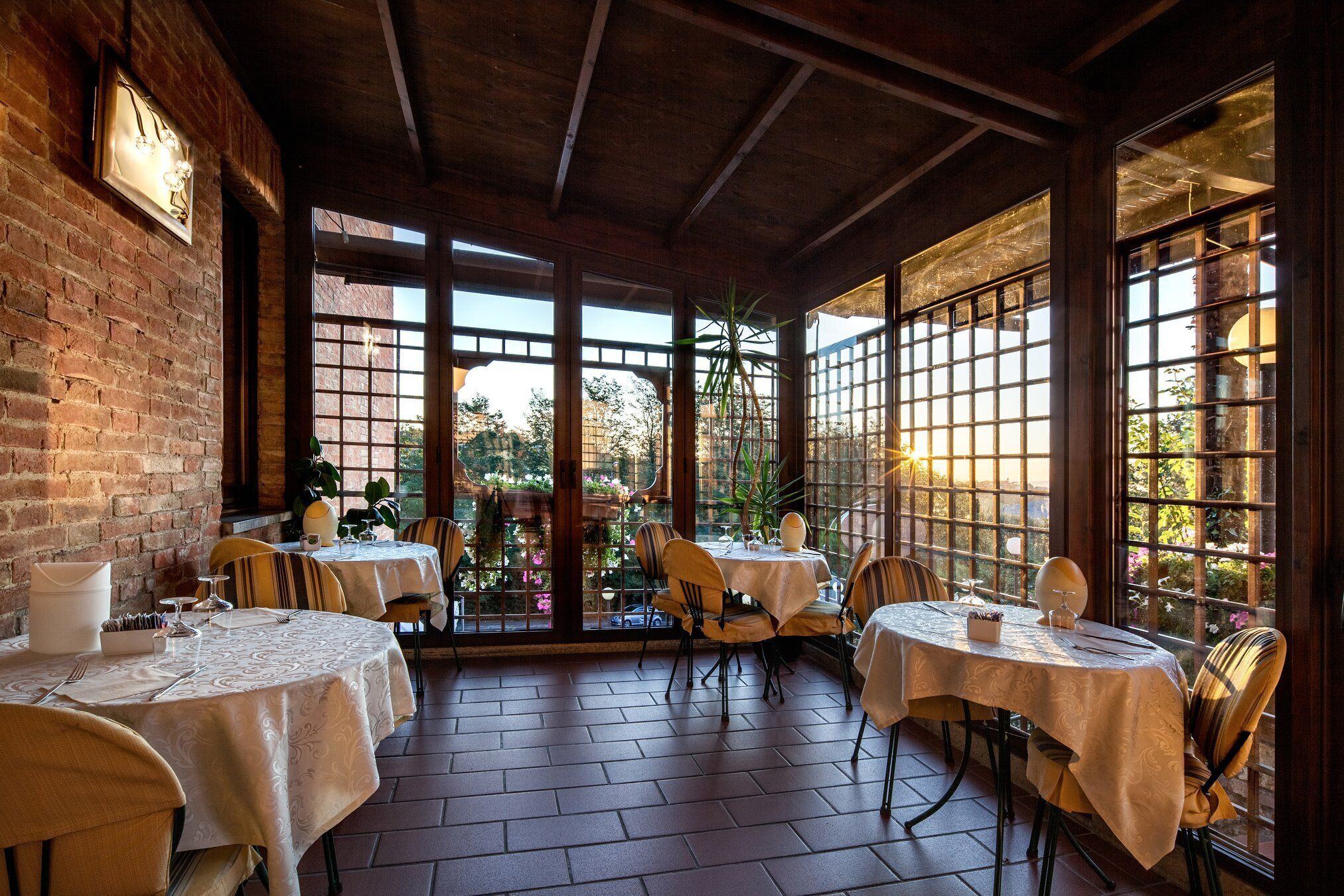 A restaurant with brick walls, large windows, and tables set for dining.