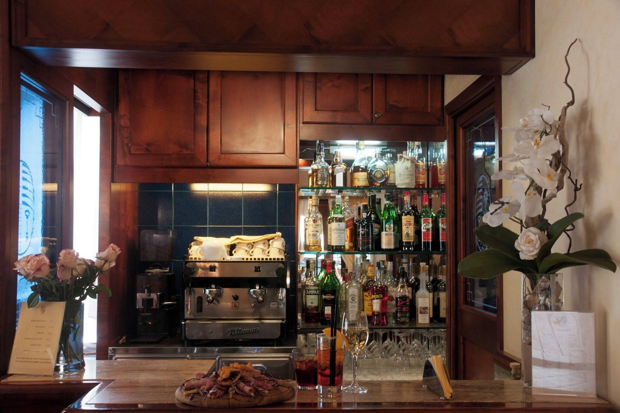 Zona de bar con armarios de madera, una máquina de café y una variedad de botellas de licores.