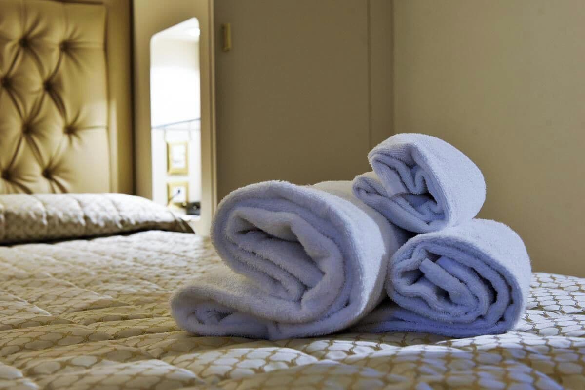 A neatly made bed with a patterned bedspread and a rolled-up towel on top.
