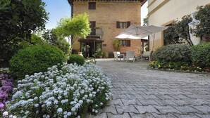 Un patio con un edificio de ladrillo, mobiliario exterior y diversas plantas.
