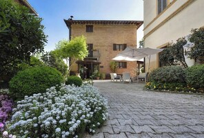 Un cortile con un edificio in mattoni, posti a sedere all'aperto e diverse piante.