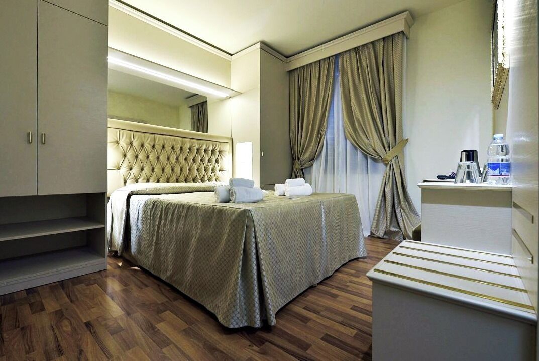 A hotel room with a bed, a bedside table, a lamp, a coffee maker, and a wardrobe.