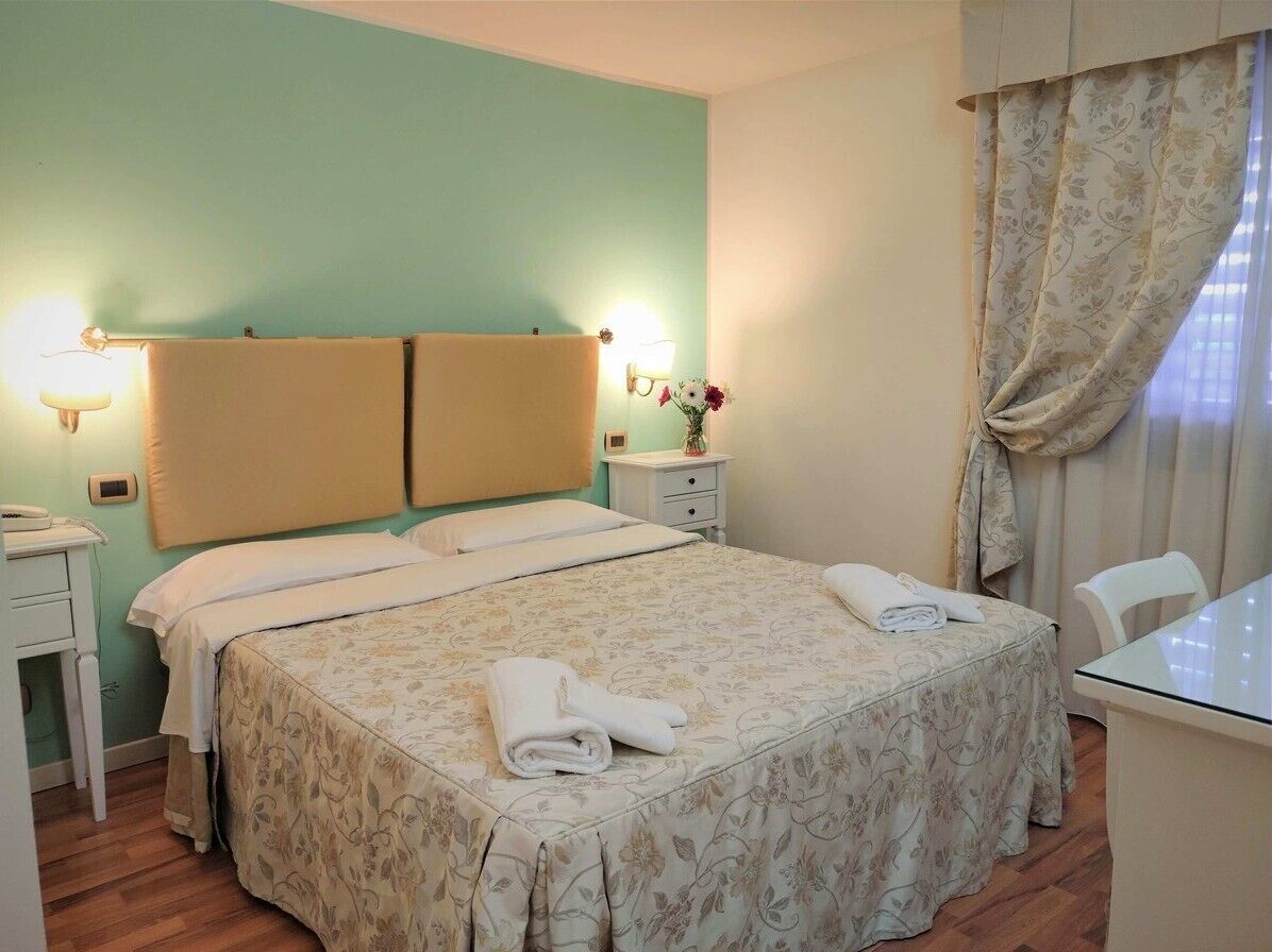 A hotel room with a bed, bedside lamps, a small table with a vase of flowers, and a chair.