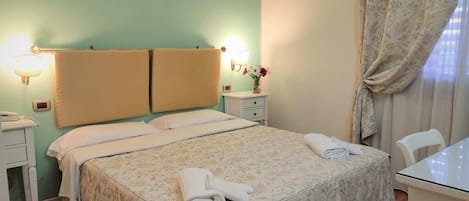 A hotel room with a bed, bedside lamps, a small table with a vase of flowers, and a chair.