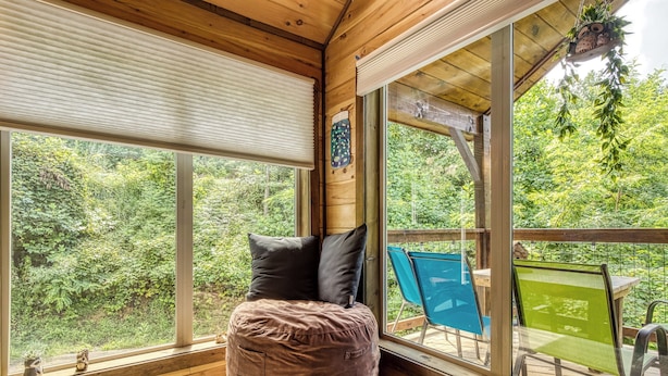Ein gemütliches Zimmer mit einem großen Fenster, einem runden Sitzsack und Blick auf eine Terrasse mit Stühlen.