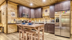 Eine Küche mit Holzwandverkleidung, dunklen Schränken, einem Edelstahl-Kühlschrank und einem Holztisch mit Barhocker.