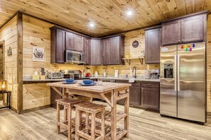 Eine Küche mit Holzwandverkleidung, dunklen Schränken, einem Edelstahl-Kühlschrank und einem Holztisch mit Barhocker.