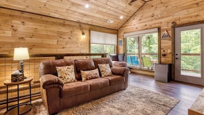 Ein gemütliches Blockhaus-Interieur mit braunem Ledersofa, Holzwänden und großen Fenstern.