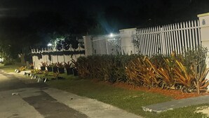 Vista nocturna de una propiedad amurallada con cerca blanca, plantas en macetas y camino de entrada pavimentado.