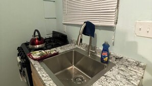 Una cocina pequeña con un lavamanos, estufa y ventana con persianas.