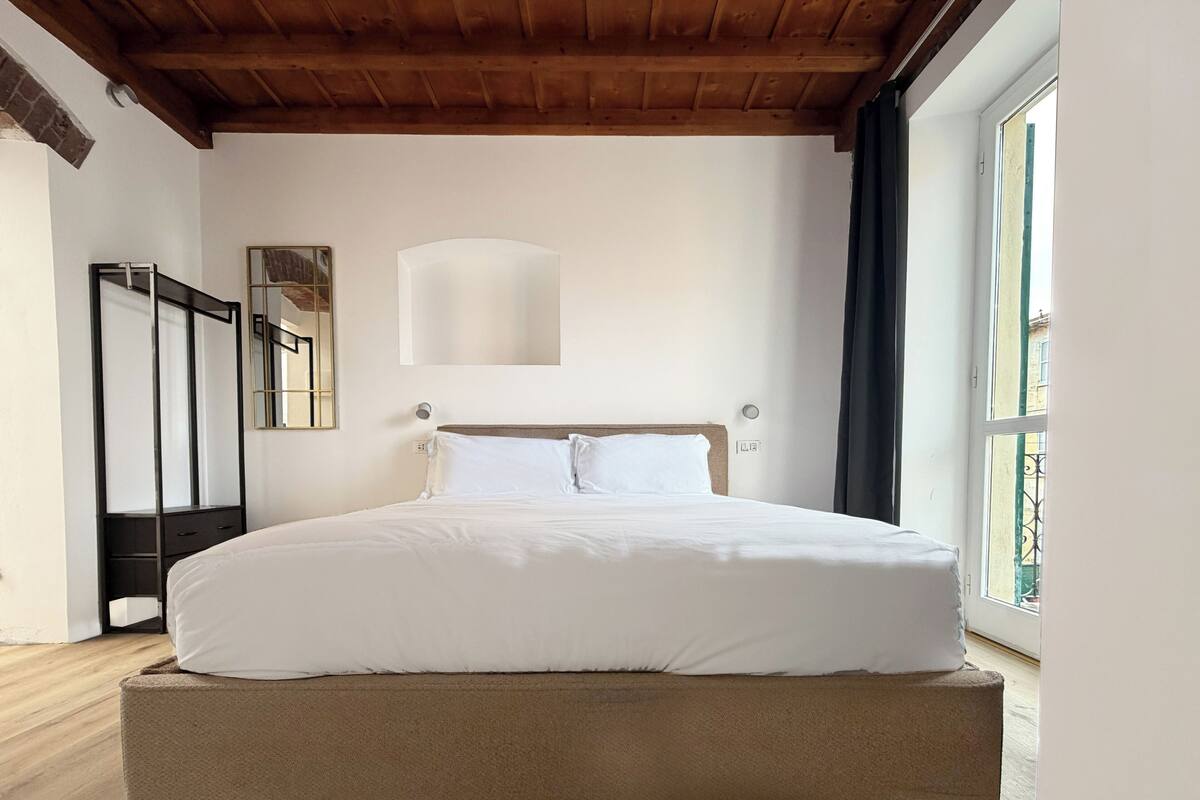 Un dormitorio con una cama grande, techo de madera, una ventana y un espejo.