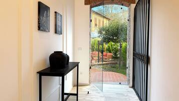 A hallway with a black table, two framed pictures, and a glass door leading to an outdoor seating area with a red bench and greenery.