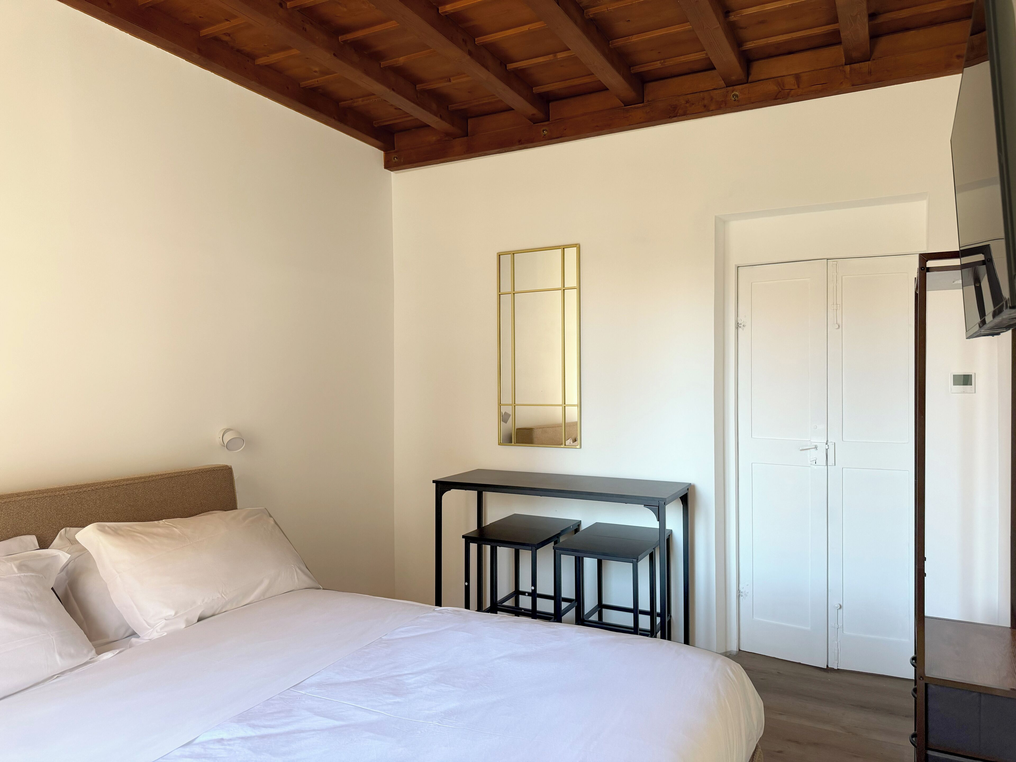 A bedroom with a bed, a desk with two chairs, a mirror, and a wardrobe.