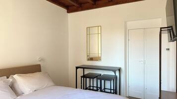 A bedroom with a bed, a desk with two chairs, a mirror, and a wardrobe.