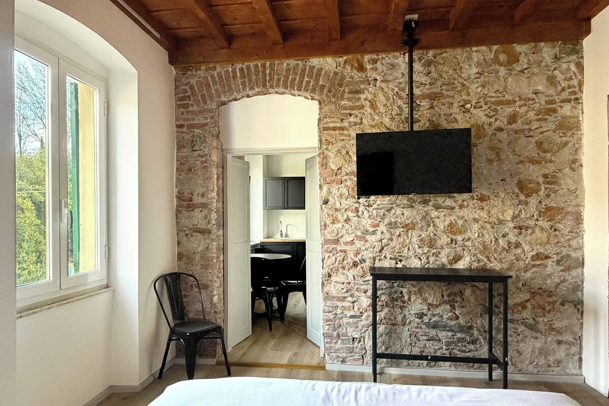 Un dormitorio con pared de piedra, una cama, un televisor montado y una silla.